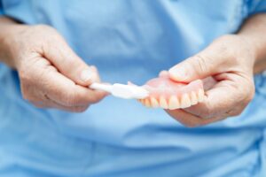 Someone cleaning a set of dentures with a white toothbrush