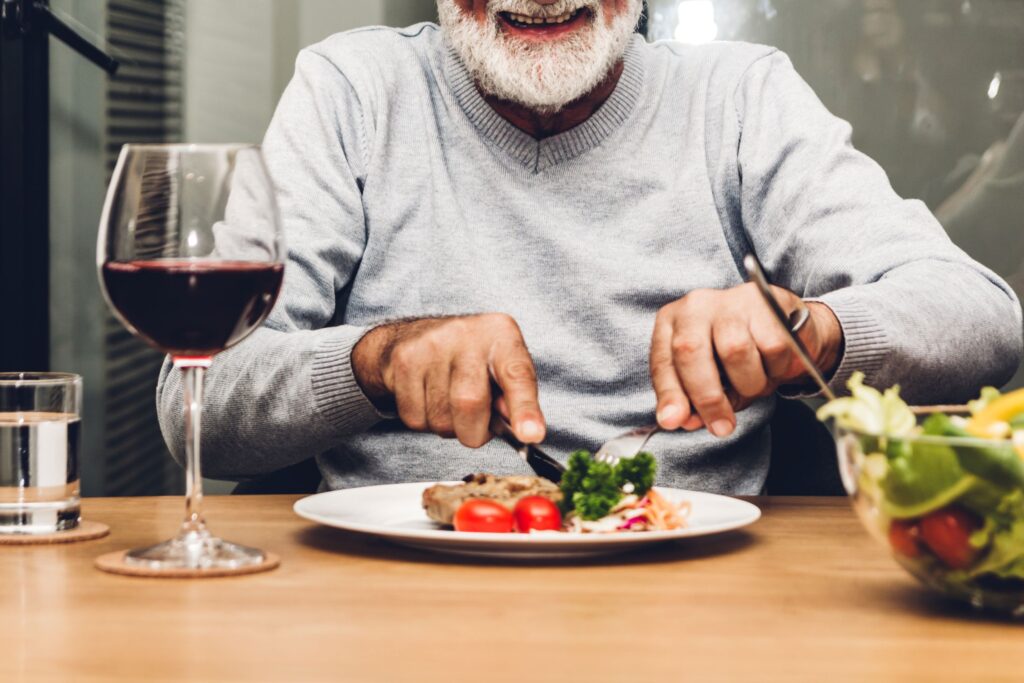 Chin-down view of man in grey sweater cutting his healthy dinner at a table